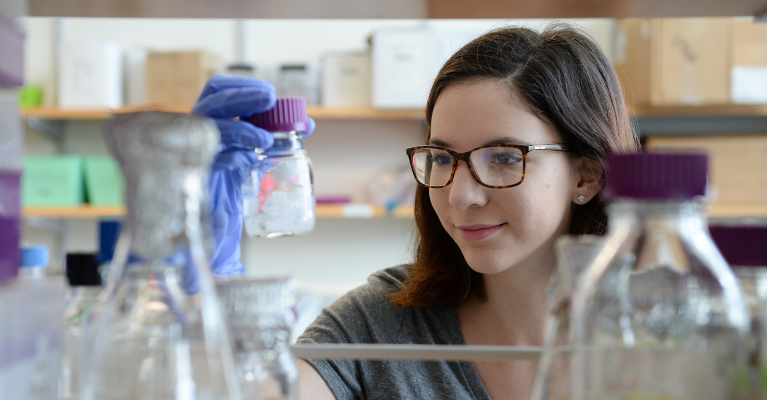 Student holding and looking at a lab container wearing gloves