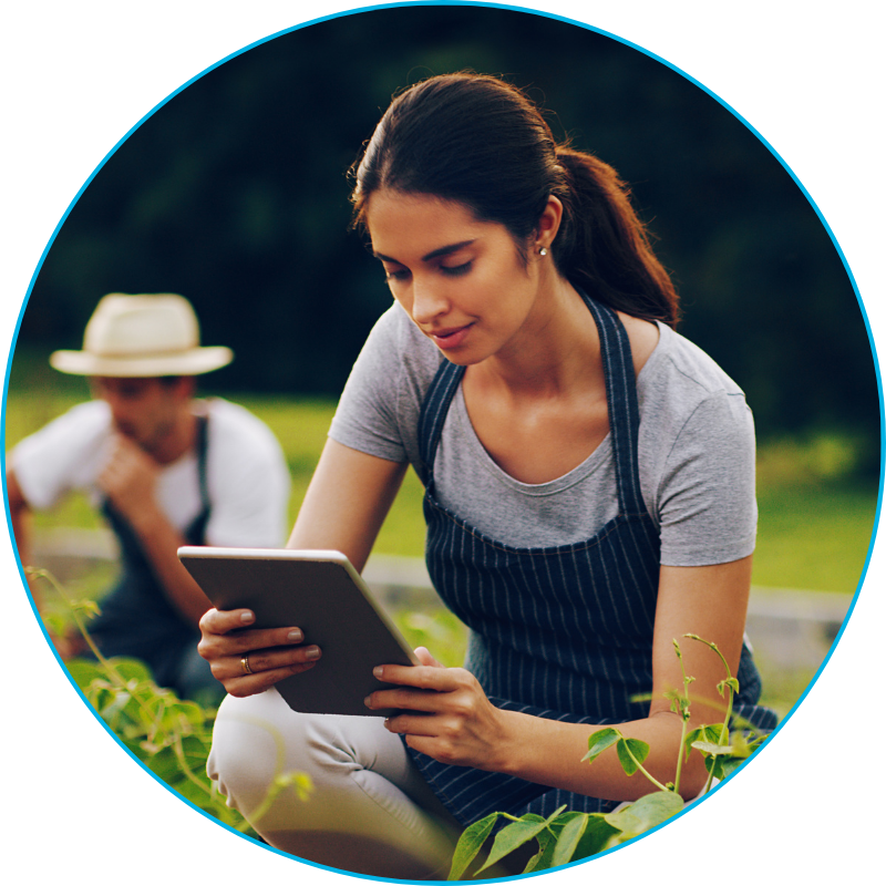 women holding a tablet kneeling next to farmed plants