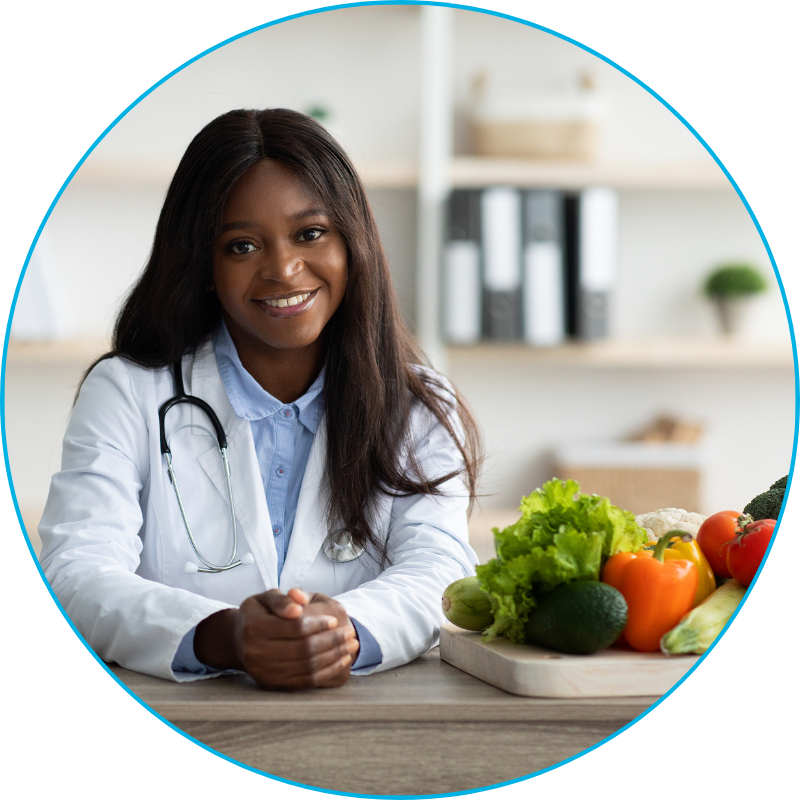 Women wearing a stethoscope at a desk with her hands cupped next to a cutting board of vegetables. 