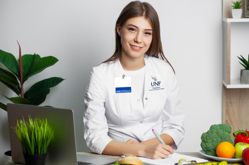 Female dietitian at a desk with a clipboard and plants behind her