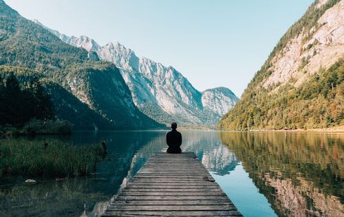 person sitting at the end of a pier with a calm lake