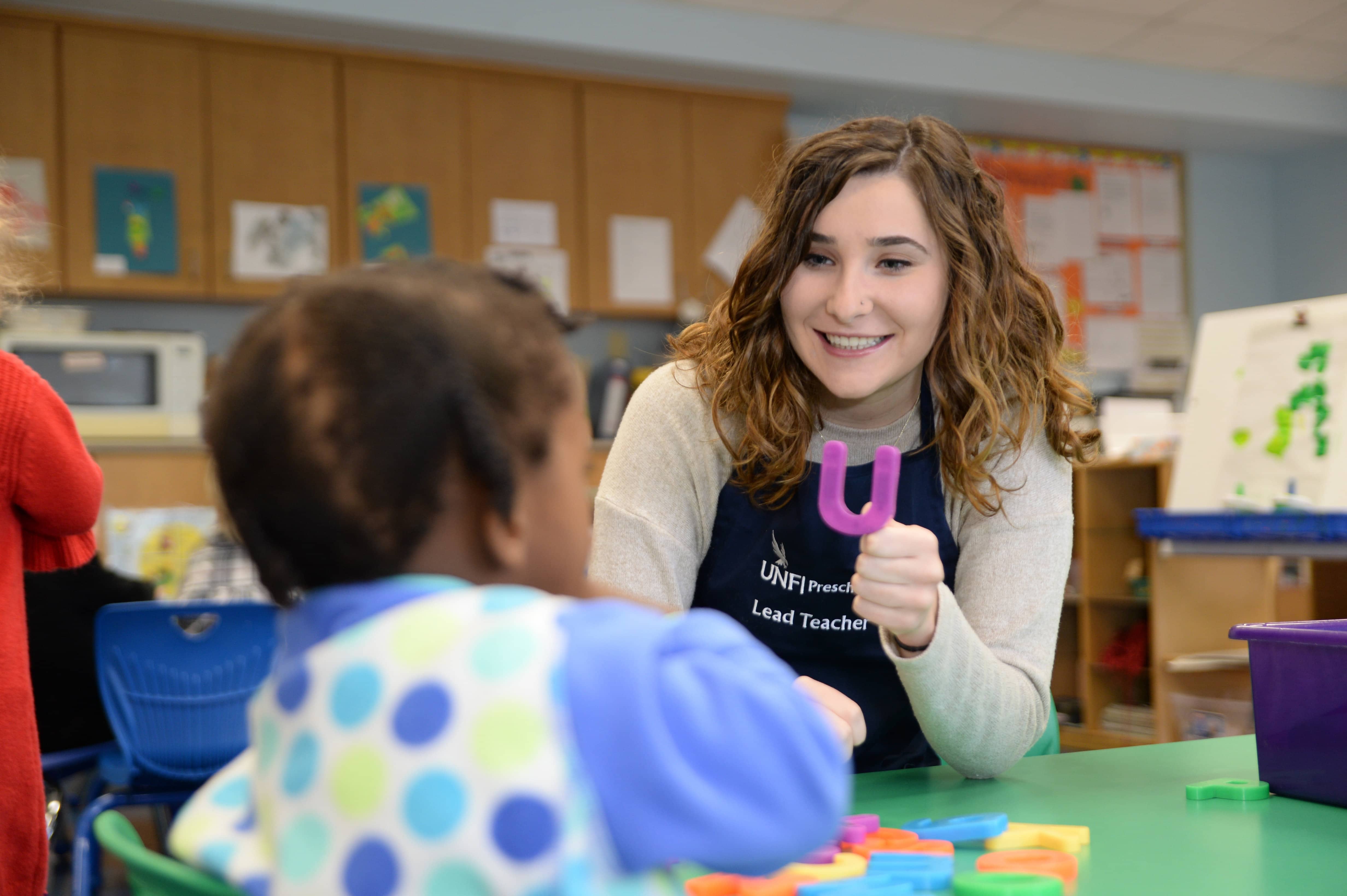 Student preschool teacher showing a letter of the alphabet to a small child.