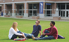 Three students sit on the grass of the UNF Green.