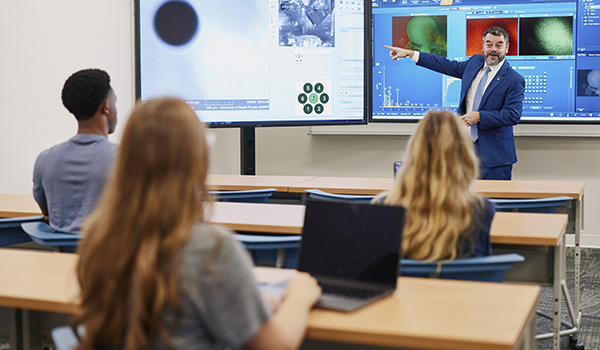 three students in a classroom while a professor teaches