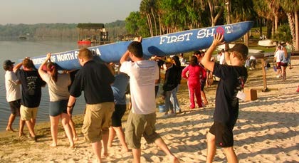 Students carrying a canoe on the beach..