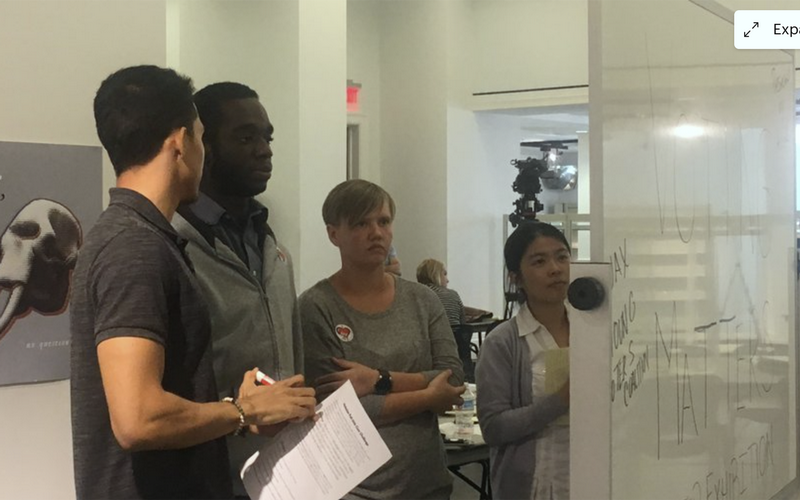 Four UNF students standing in front of and looking at dry-erase board.png