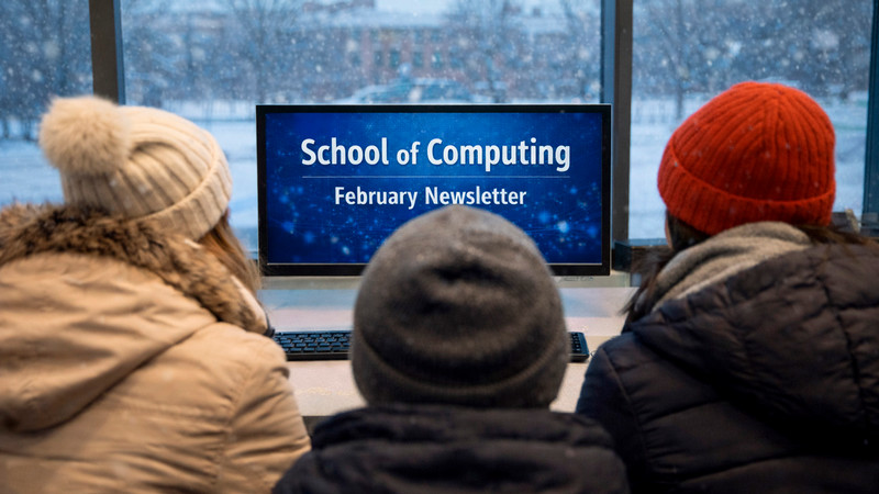 Students looking at computer monitors, one with "School of Computing February Newsletter" on it