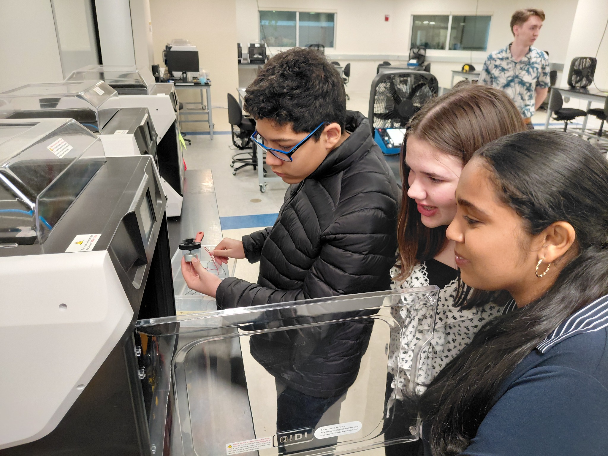 three students looking into a 3d printer, one with an electric motor in his hands.
