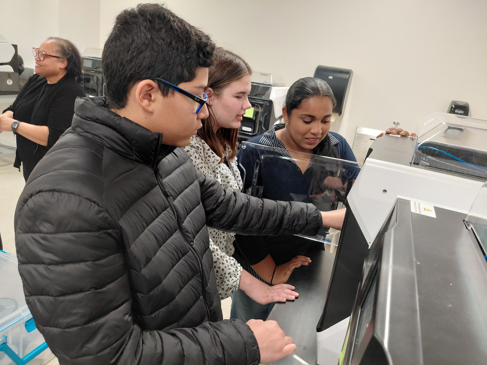 student reaching into 3d printer with two students watching and a parent in the backround