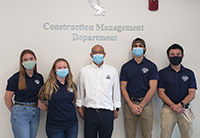Two women and three men all wearing masks under a sign for the construction management department