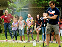 two students demonstrating a rocket with a group of young girls