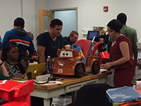 two students working on an adaptive toy with other people in the background