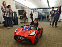 a boy in an adaptive toy car with people in the background