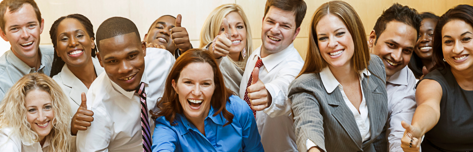 group of diverse employess leaning forward and smiling with their thumbs up