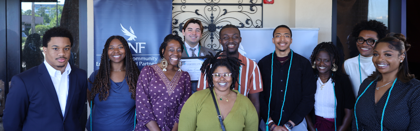 A group shot of smiling individuals with some wearing a graduation cord