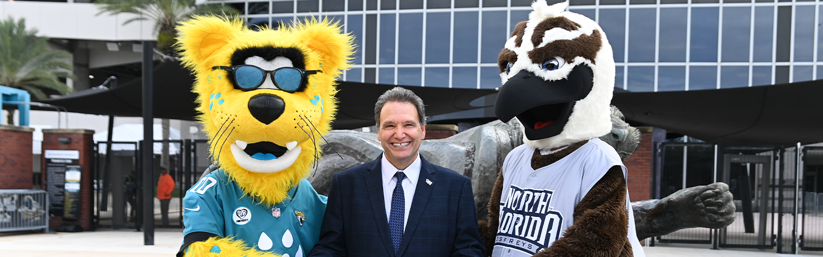 Ozzie, President Limayem, and Jaxson de Ville taking a photo in front of the EverBank Stadium