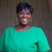 Angela smiling and wearing green blouse, golden link necklace with ring, and gold ring earring