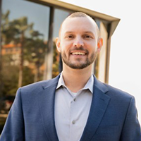 Chris smiling and wearing a blue suit with a light blue button-up shirt