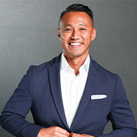 Delonyx smiling with his hand buttoning his blue suit jacket that in a handkerchief in the pocket