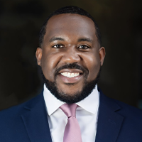 James smiling wearing a dark blue suit with silver tie