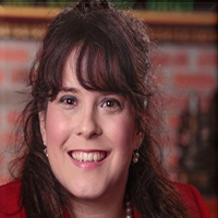Kara smiling and wearing a red suit jacket and pearl earrings