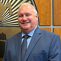 Keith smiling and wearing a blue suit with a light blue undershirt and black pattern tie