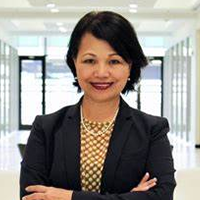 Penny Zuber wearing a black suit jacket, checker pattern blouse, and white pearl necklace