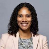 Whitney is wearing a beige suit jacket, colorful blouse, and a necklace