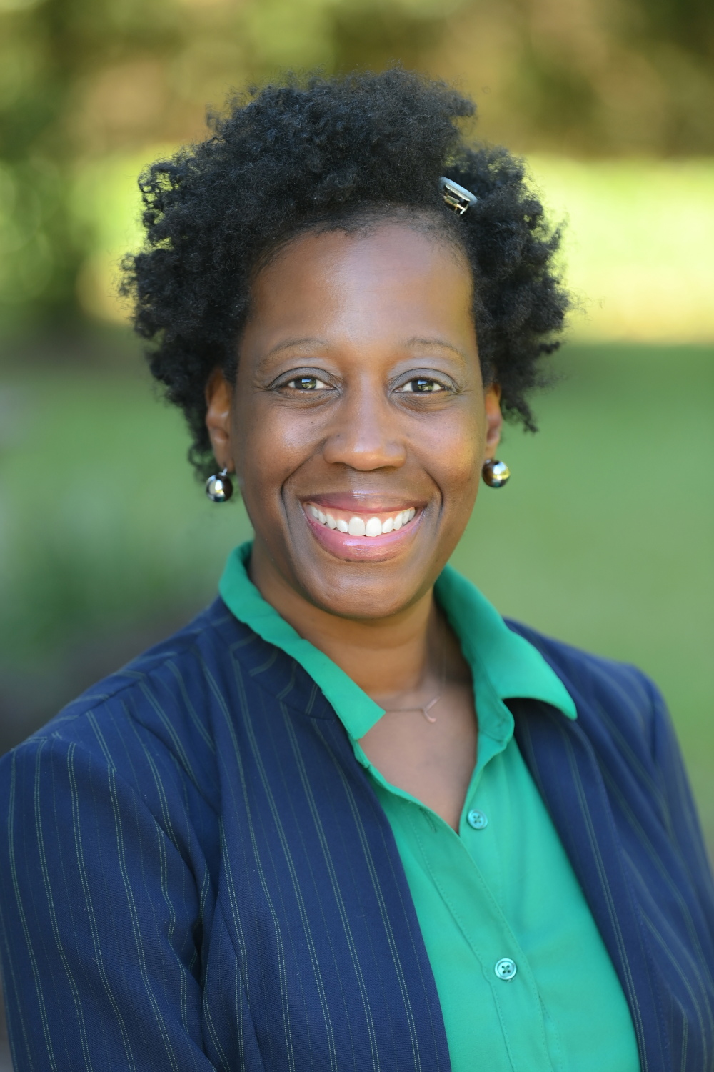 Jacinda smiling and wearing an open blue suit coat on top of a green button-up shirt