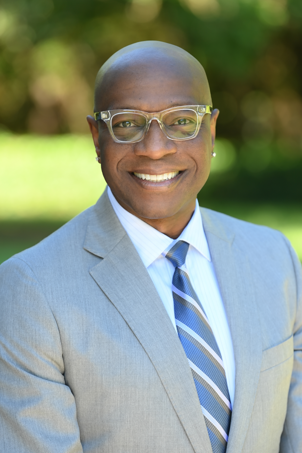 Richmond smiling and wearing a gray suit, blue tie, and glasses