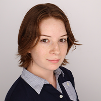 Anne smiling and wearing a blue button collar shirt with the inner color being gray