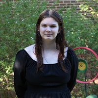 Elise wearing a black dress and smiling with a nature and brick background