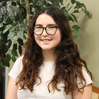Hannah smiling and wearing glasses and white top