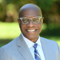 Richmond smiling and wearing a gray suit, blue tie, and glasses