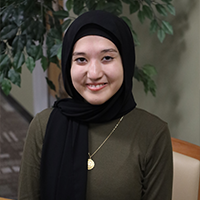 Tayebe smiling wearing a green shirt, black hijab, and gold necklace