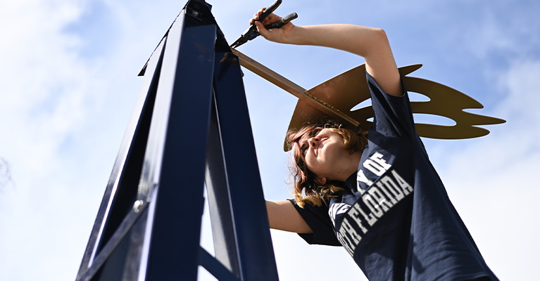Student working on the top of a sculpture in the sculpture park