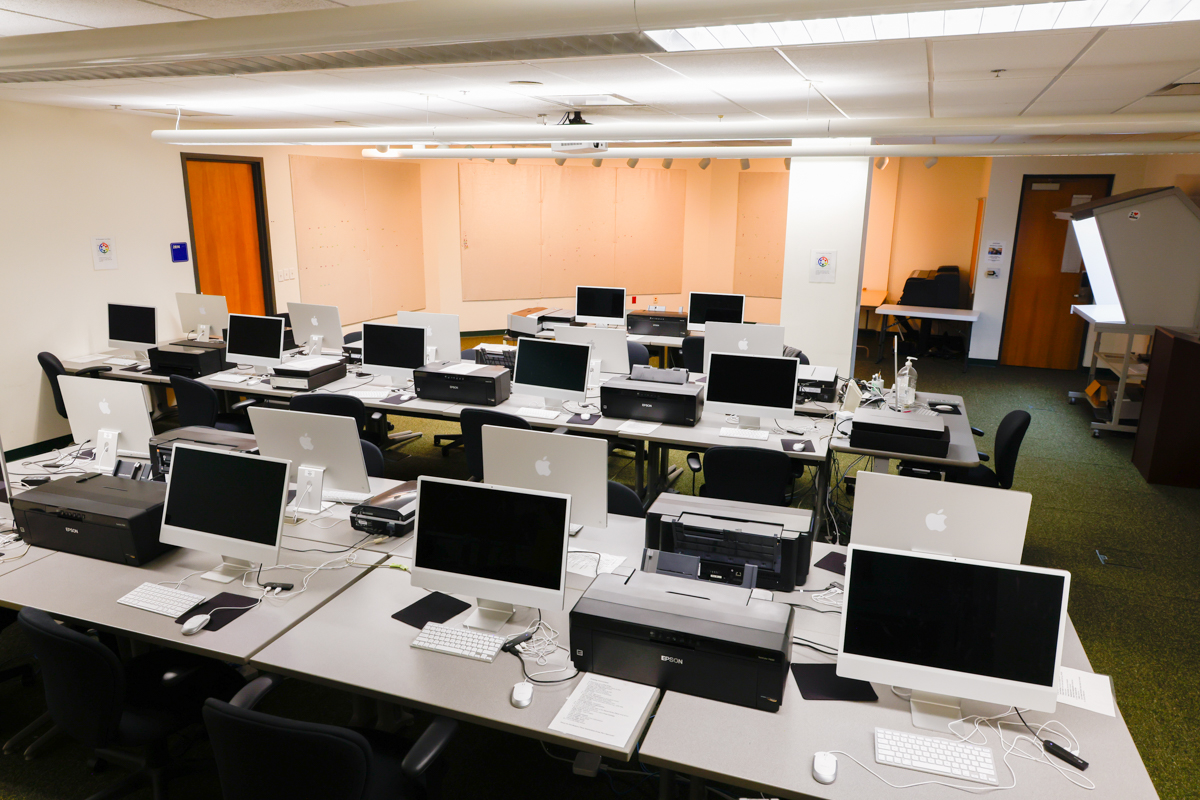 Classroom with Mac computer workstations and printers.