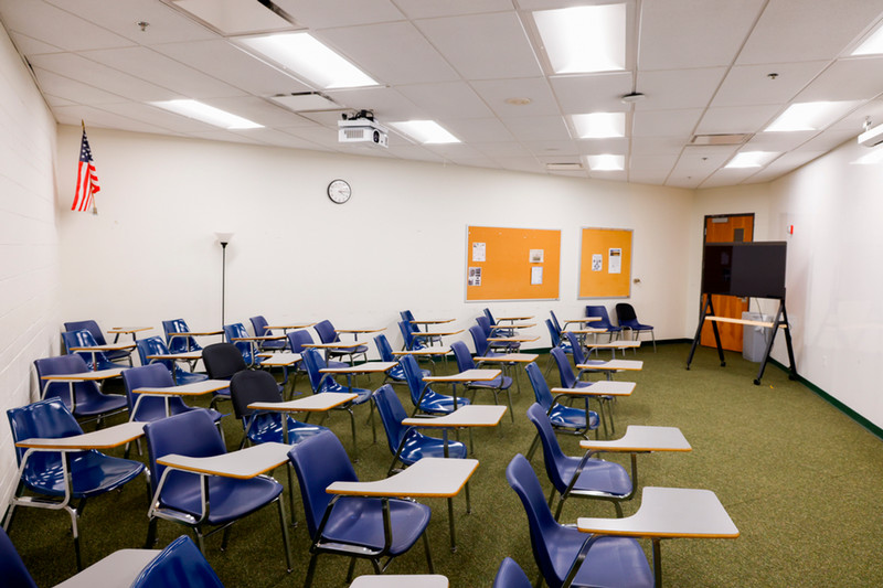 Empty classroom with blue chairs, desks, a projector and wall clock.
