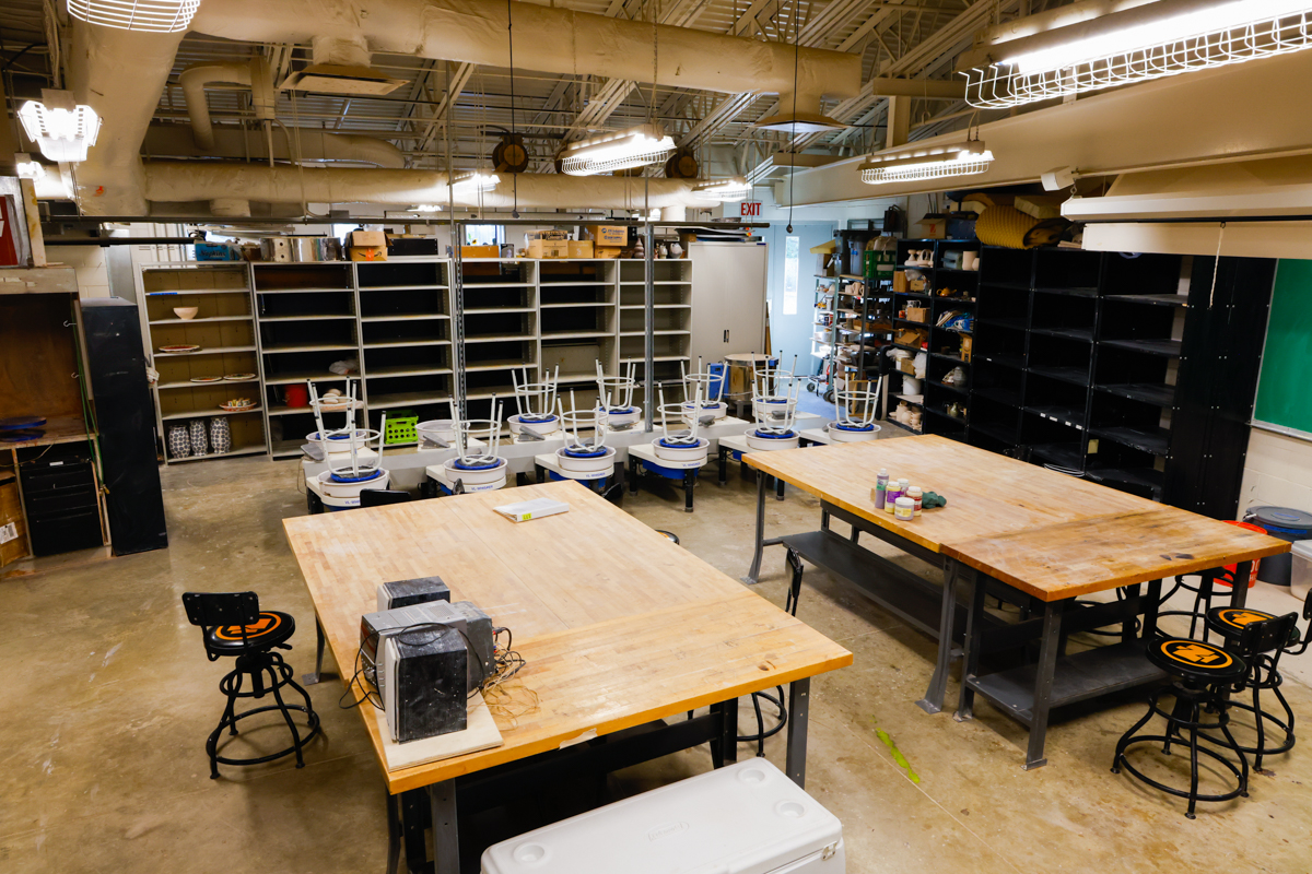 Spacious art classroom with large tables, storage shelves and empty stools.