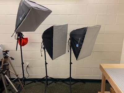 Three softbox lighting setups on stands in a studio.