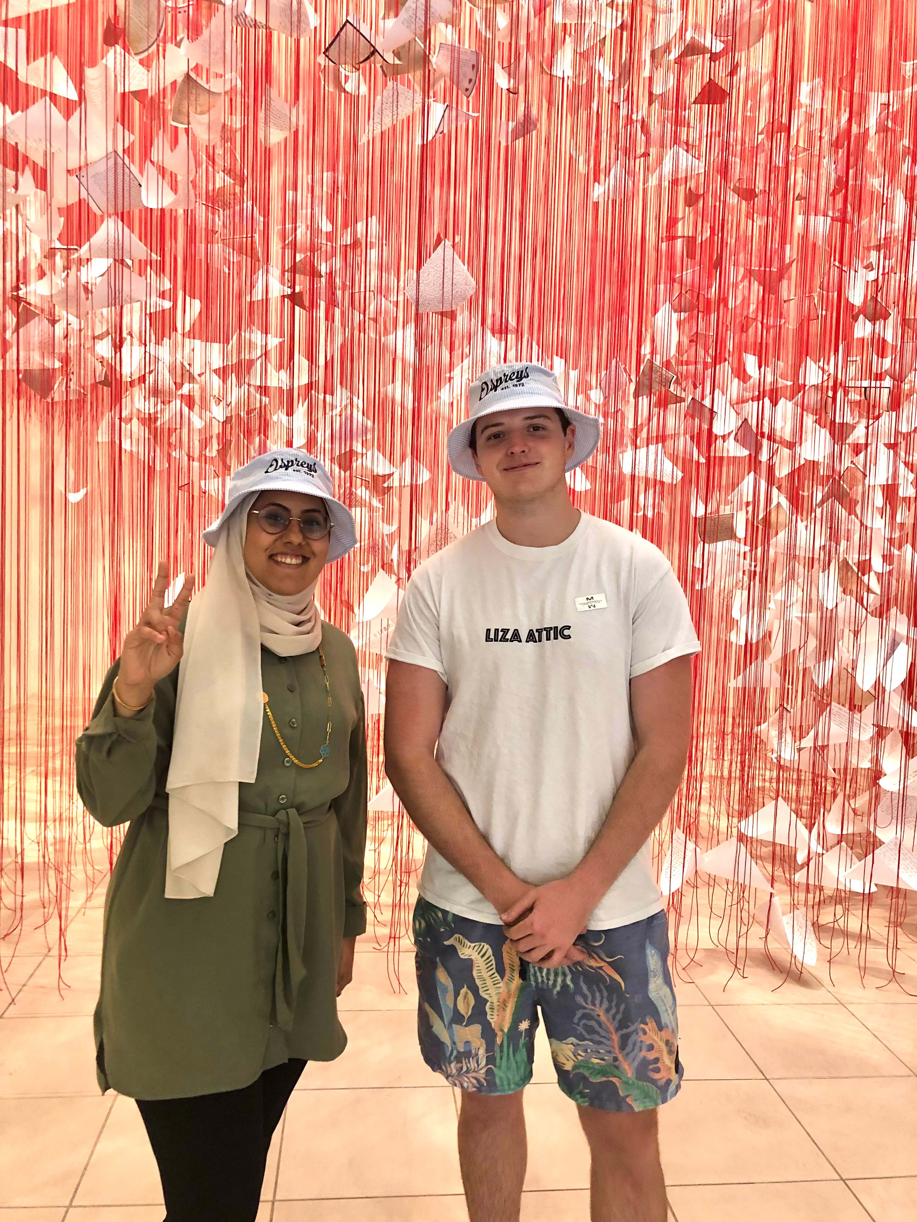 Two friends posing together in front of a vibrant red and white backdrop wearing matching bucket hats