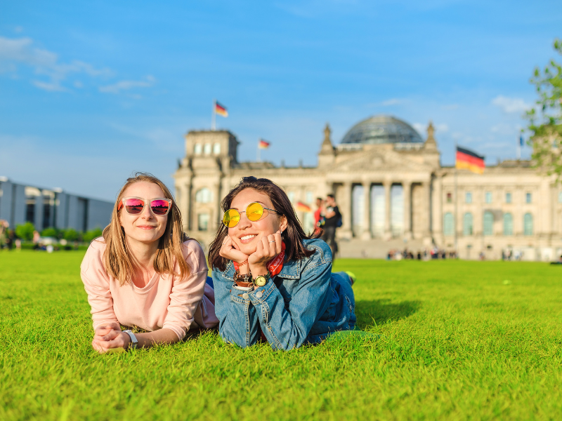 Two UNF students studying abroad seated on grass near historic architecture
