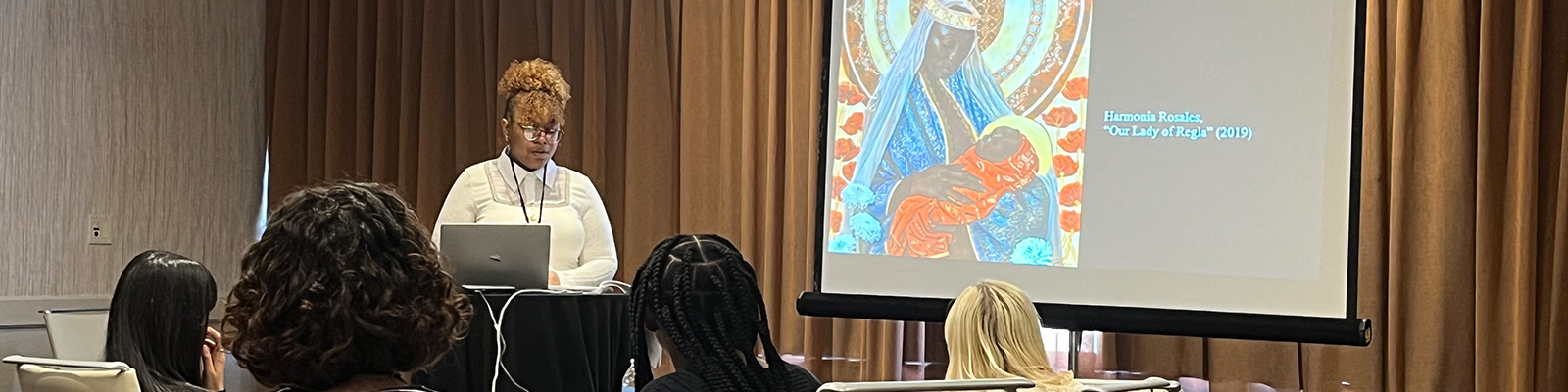 A speaker presents on the importance of art, with an artwork display titled The Lady in Red by Hemena Harris in the background.