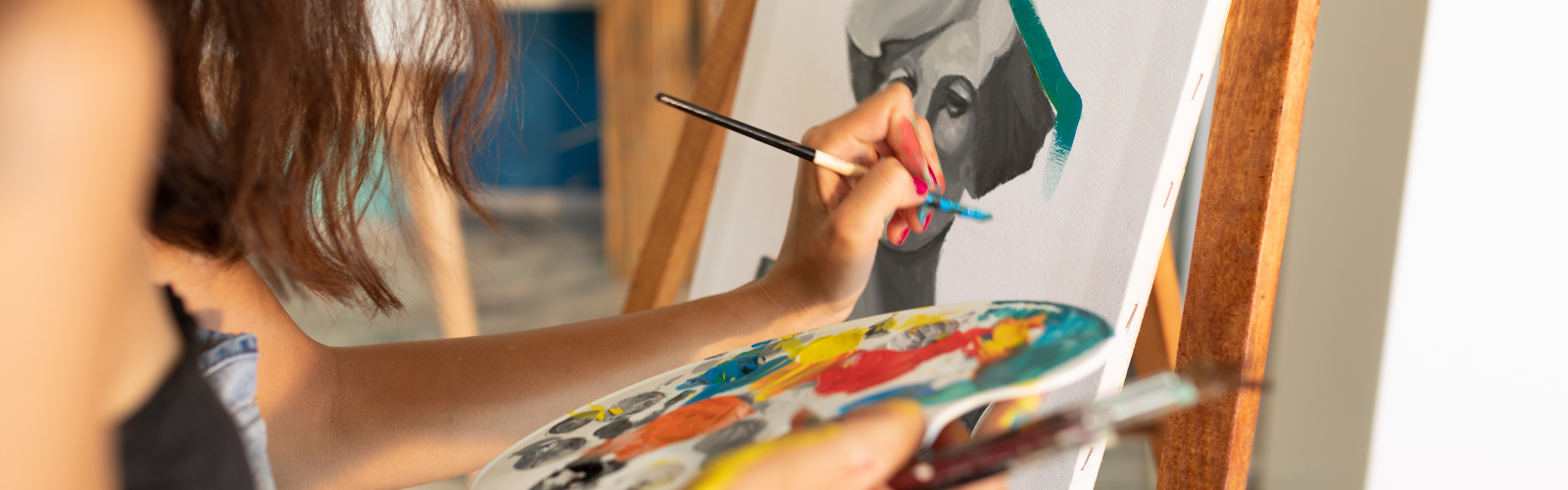 Student painting a portrait on canvas with a brush and palette in a fine arts studio