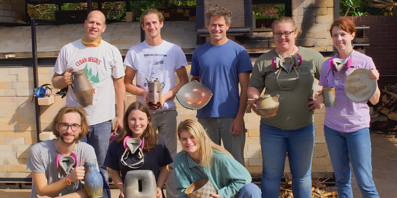 Group of students holding ceramic pieces and tools outside a kiln area in a sculpture studio