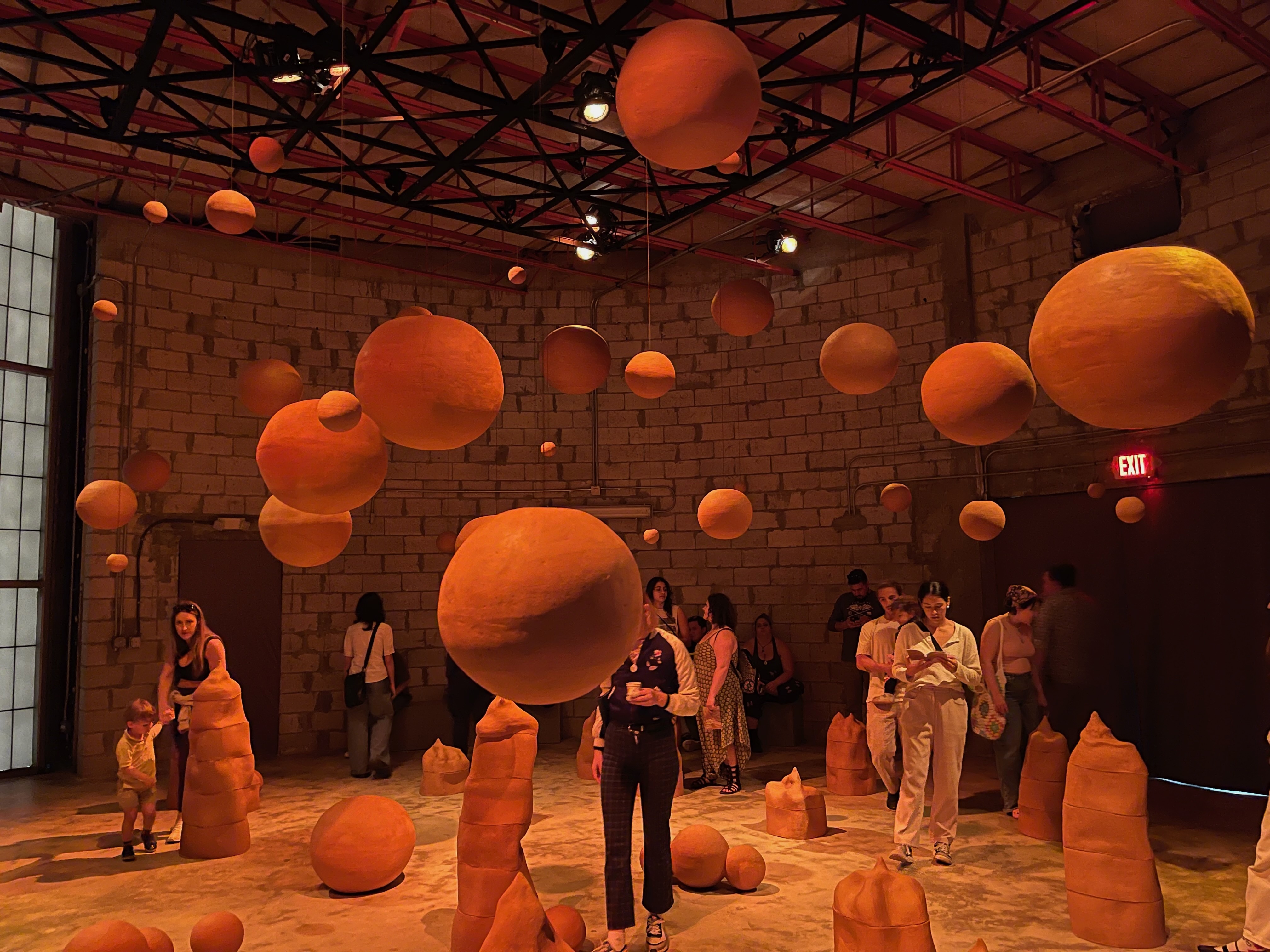 Visitors exploring an immersive art installation featuring suspended clay forms in a spacious gallery