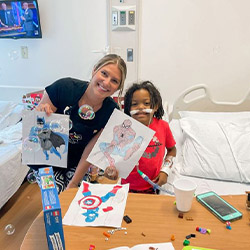 kid in a hospital bed drawing superheroes with university student