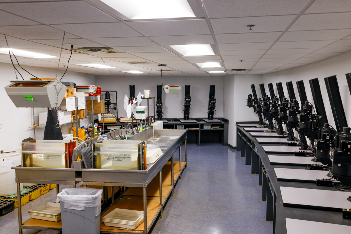A bright and organized photo processing lab featuring multiple workstations equipped with film projectors and a central processing counter.