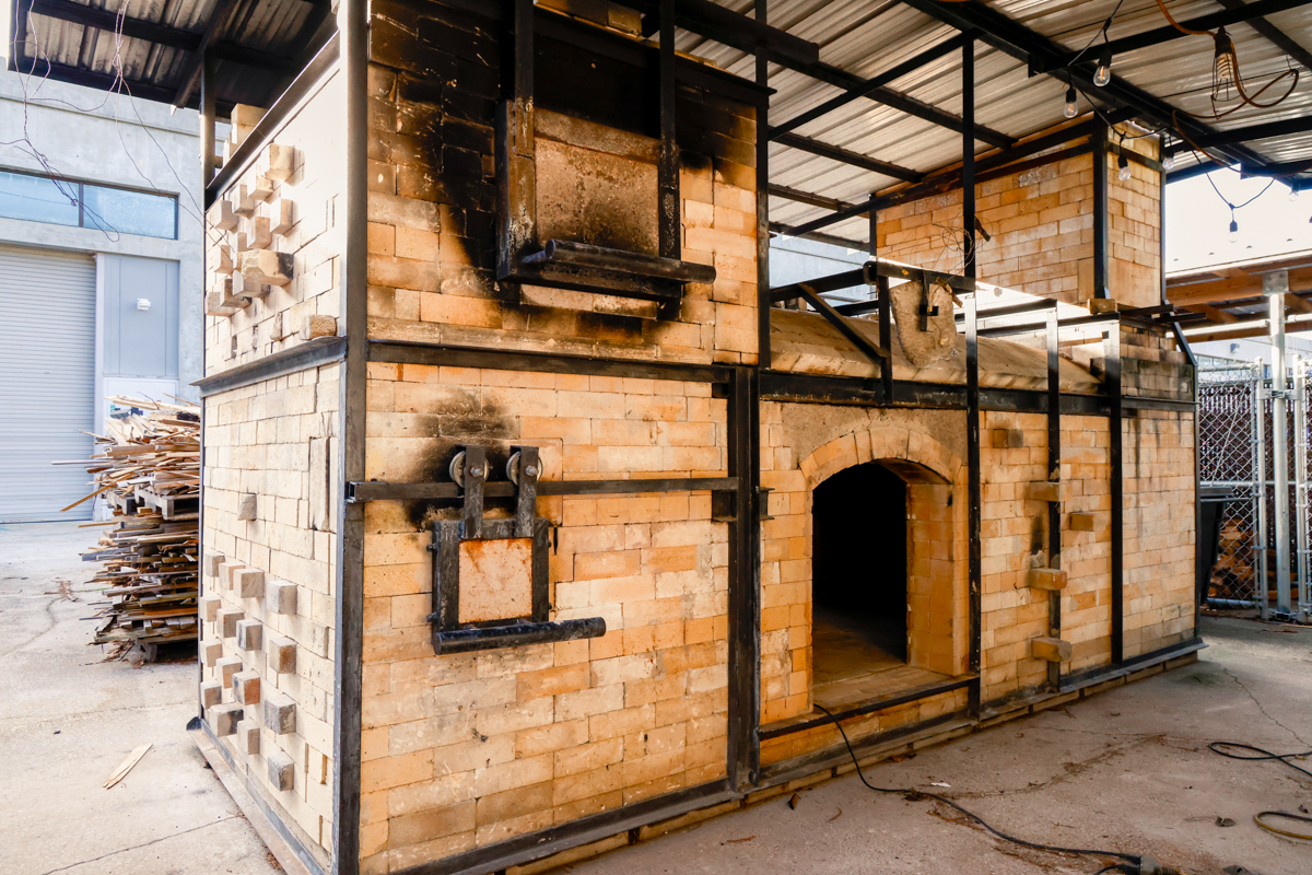 A large, industrial-style brick oven with a black metal frame, located outdoors, showcasing its sturdy construction.