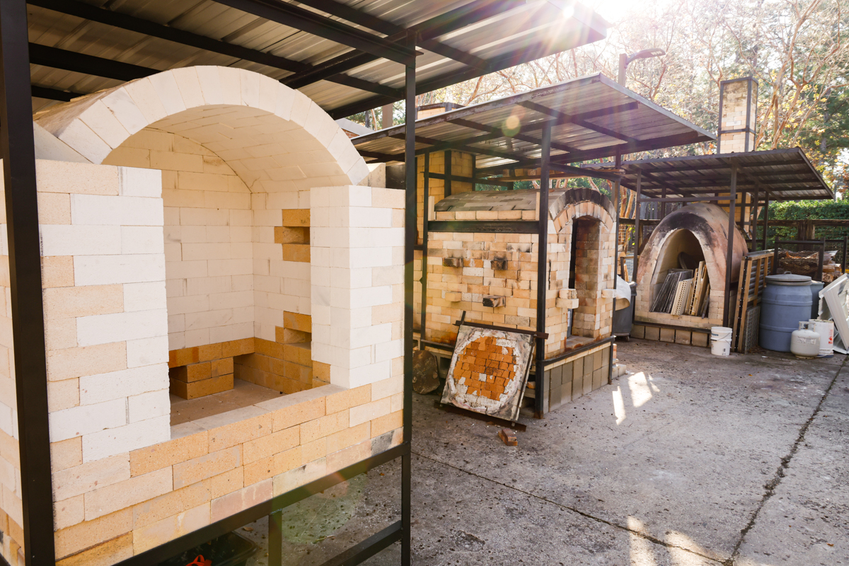 A view of several kiln structures made of bricks and steel frames, set in a workshop with natural lighting.
